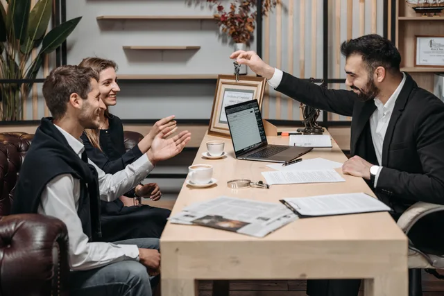 Business professional handing keys to smiling clients at an office desk during a consultation. Property creators return on investment: a framework