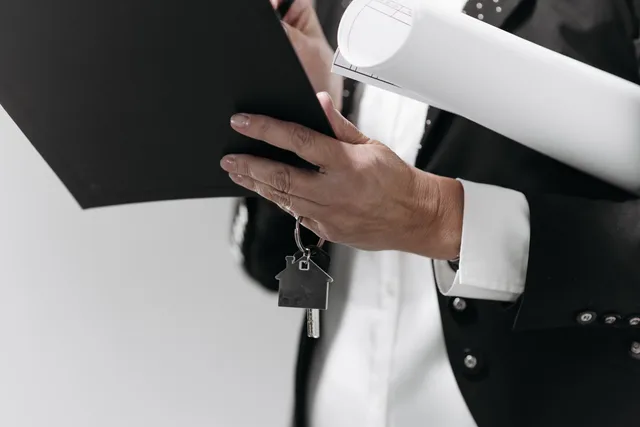 Close-up of a business professional holding a house key and architectural plans, symbolizing real estate. Property creators vendor due diligence: evidence gates
